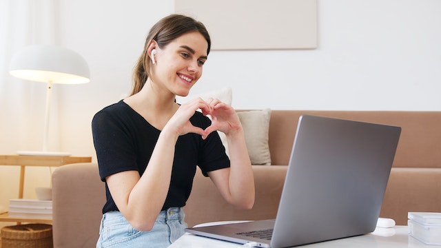 woman giving heart sign video chat on laptop