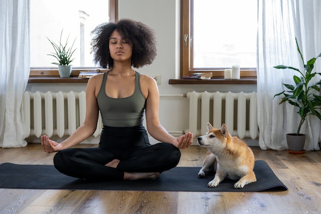 woman with curly hair meditating on yoga mat with dog
